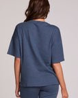 Back view of a woman wearing the Chaser Lunnah Dark Denim Top and blue pants on a neutral background