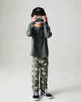A full body front view of a boy wearing the Chaser Monster Truck Pants Boys Jogger on a neutral background holding a camera
