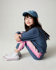 Front view of a seated girl wearing the Chaser Multi Stripes Girls Hoodie on a neutral background with hat and matching pants