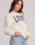 Side angle view of a woman wearing the Chaser Navy Love Pullover Sweater and jeans on a neutral background