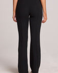 Back view of a woman wearing the Chaser Rhose Black Pants on a neutral background with arms lowered down sides