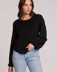 Front view of a woman wearing the Chaser Ruthy Black Fullsleeve Top on a neutral background with jeans, one hand on hem and another in pocket