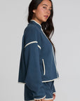 Side view of a woman wearing the Chaser Sharun Dark Denim Jacket and shorts on a neutral background