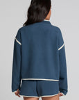 Back view of a woman wearing the Chaser Sharun Dark Denim Jacket and matching shorts on a neutral background