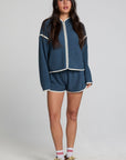 Full body front view of a woman wearing the Chaser Sharun Dark Denim Jacket and matching blue shorts on a neutral background