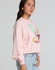 Side view of a woman wearing the Chaser Sporty Patches Long Sleeve Top and blue jeans on a neutral background