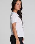 Side view of a woman wearing the Chaser Sun Records Elvis 1972 Tee on a neutral background with arms at sides and pants