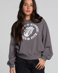 Frontview of a woman wearing the Chaser The Rolling Stones 78 Tour Cropped Sweatshirt on a neutral background with black pants an d hand in pocket