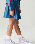 Side view of a girl wearing the Chaser Tiny Hearts Girls Skirt on a neutral background with arms lowered