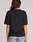 Back view of a woman wearing the Chaser Woodstock Bird on Guitar Tee on a neutral background and jeans