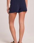 A back view of a woman wearing the Chaser Evie Admiral Shorts and shoes on a neutral background