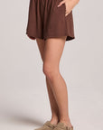 A side view of a woman wearing the Chaser Kahlua Harper Shorts on a neutral background with her hands in her pockets