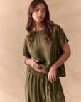 Woman wearing the Davis tee in bronze green against a beige background with matching Lee Pants