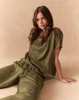 Woman wearing the Davis tee in bronze green sitting on a beige background with matching Lee Pants