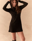 Front view of model in Merced Hoodie Dress in True Black with hood up against a beige background