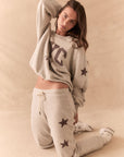 Full body view of model wearing NYC Stars Pullover in Heather Grey with black star sleeves and matching joggers, styled casually, against a beige background
