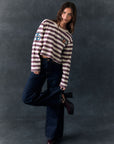 Full body view of model standing against a dark background wearing The Rolling Stones Rugby Stones Logo Long Sleeve with red and white stripes, cropped fit, tongue logo graphic, and jeans