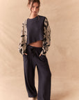 Full body view of Woman wearing a patterned cardigan over a crop top and wide-leg pants on a beige background