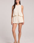 Full shot of a woman in a matching tank and shorts set and green shoes on a neutral background