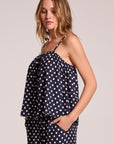 Side angle view of a woman wearing the Chaser Rubie Navy Spot Tank Top on a neutral background with hands in her pockets
