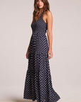 Side angle view of a woman wearing the Chaser Siren Navy Spot Maxi Dress on a neutral background with one foot raised