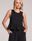 Front view of a woman wearing a black Chaser Liberty tank set with her hands in her pockets on a neutral background