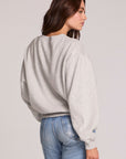 Back view of a woman wearing the Chaser The Rolling Stones Long Sleeve Tee on a neutral background with hand on one hip and jeans