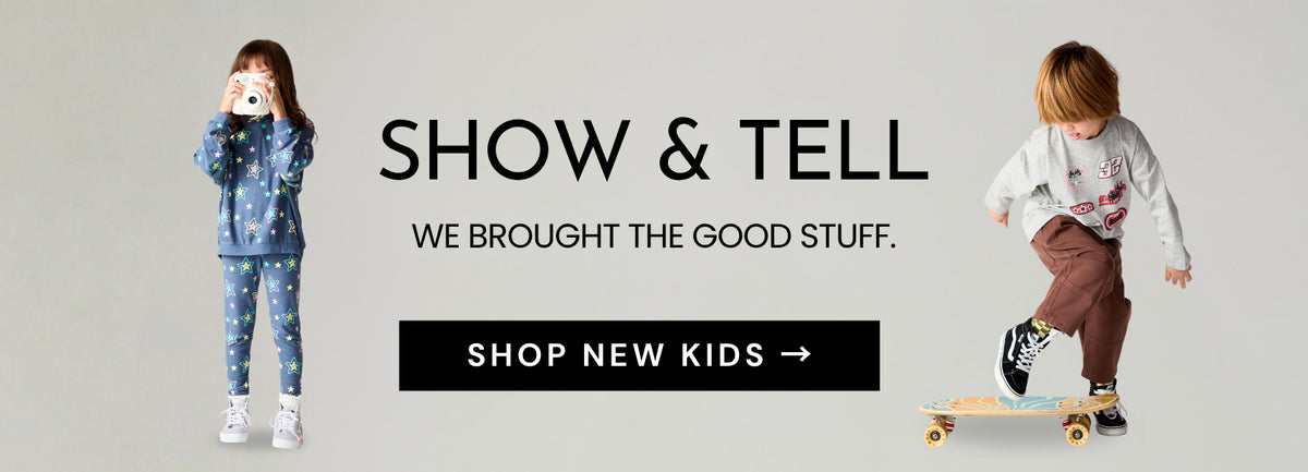 A promotional banner for children's apparel featuring two kids modeling outfits against a light gray background. On the left, a girl in a blue patterned long-sleeve top and matching pants holds a camera