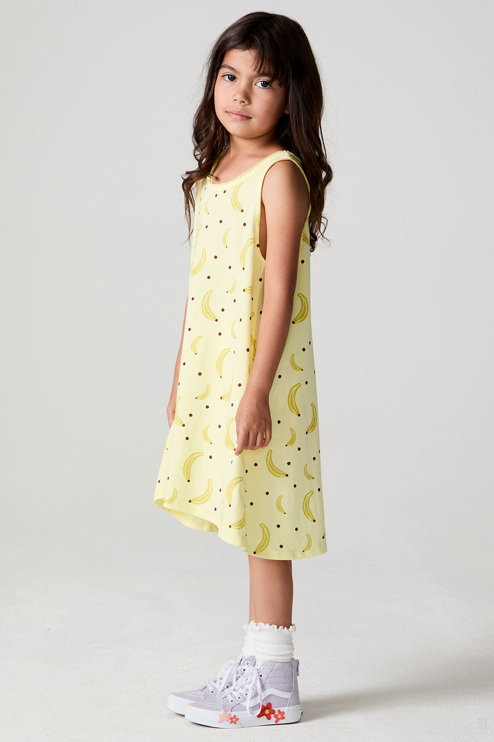 Full body side view of a girl wearing the Chaser Banana Babe Dress and sneakers on a neutral background