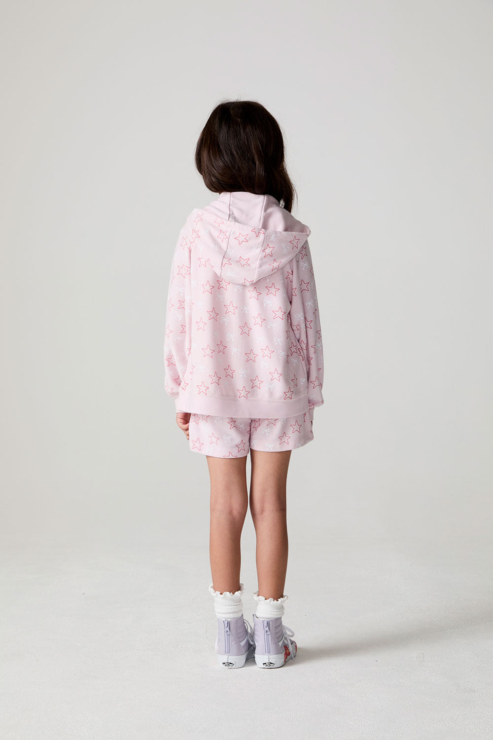 Back view of a girl wearing the Chaser Bows and Stars Zip-Up on a neutral background