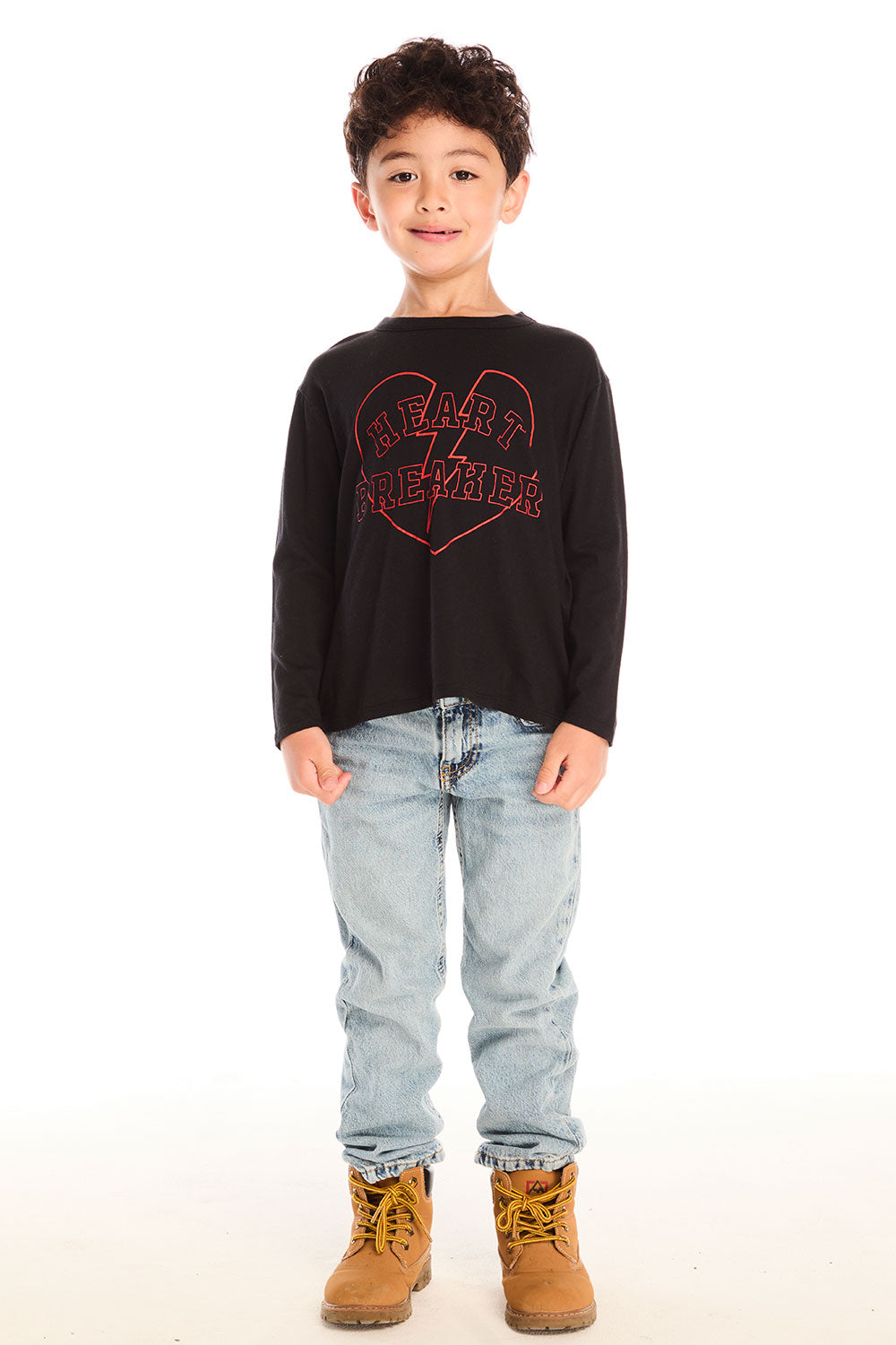 Full body view of boy wearing Chaser’s Heartbreaker black long-sleeve shirt with red text, broken heart graphic, light blue jeans, and brown boots on a white background