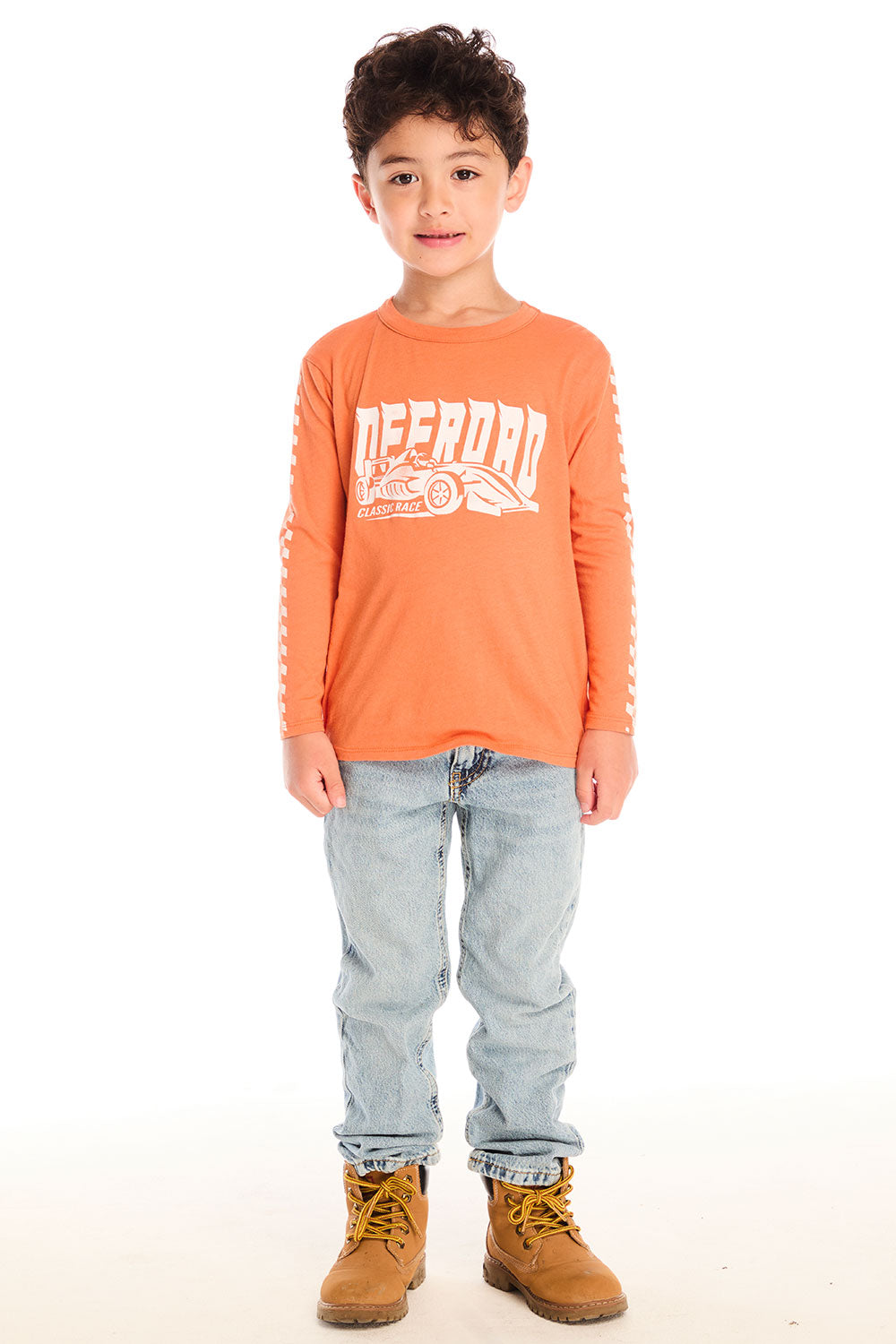 Full body view of boy wearing Chaser’s Raceway Speed orange long-sleeve top with a race car graphic and light blue jeans on a white background