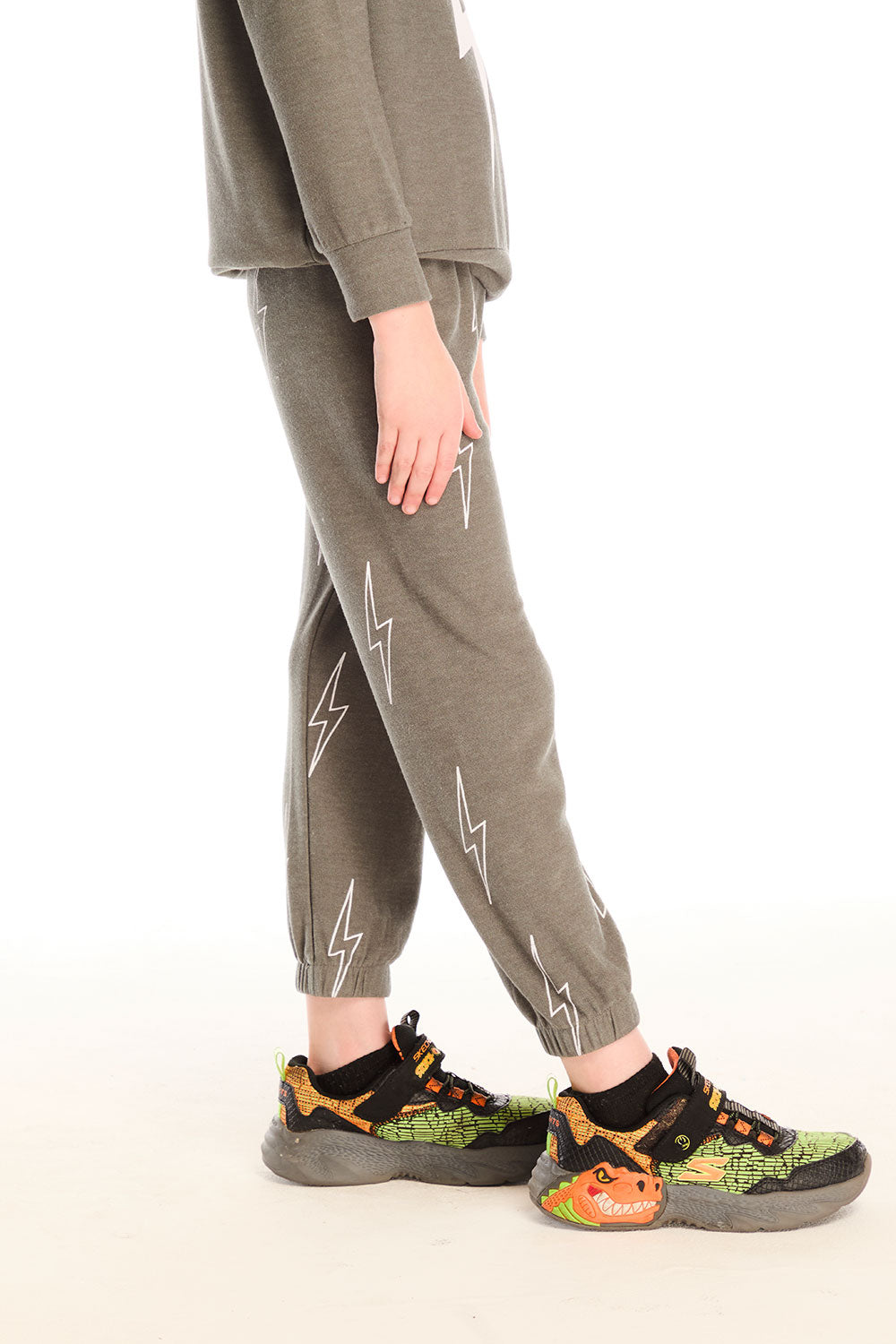 Side view of boy wearing Chaser's green Allover Bolts Pants with lightning bolt designs on a white background