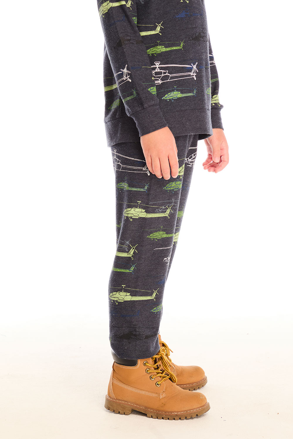 Side view of boy wearing Chaser's dark gray Allover Helicopters pant with green airplane patterns and matching top on a white background