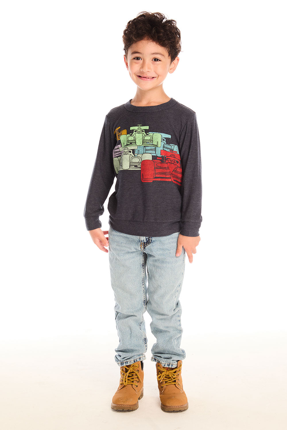 Boy wearing Chaser's Allover Racing dark gray sweatshirt with colorful graphic design, light blue jeans, and brown boots on a white background