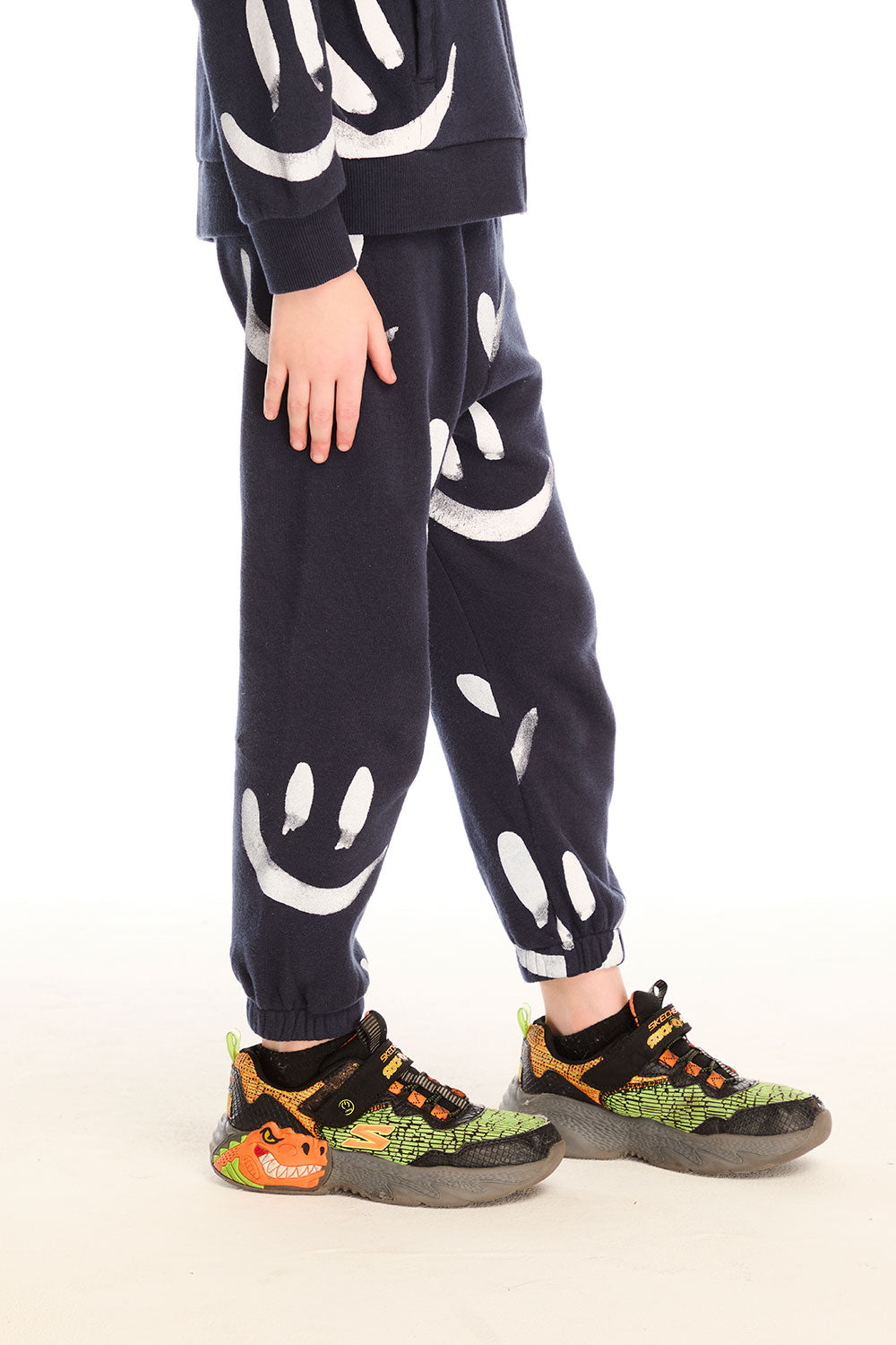 Side view of boy wearing Chaser's navy Allover Smileys Pants with white patterns on a white background