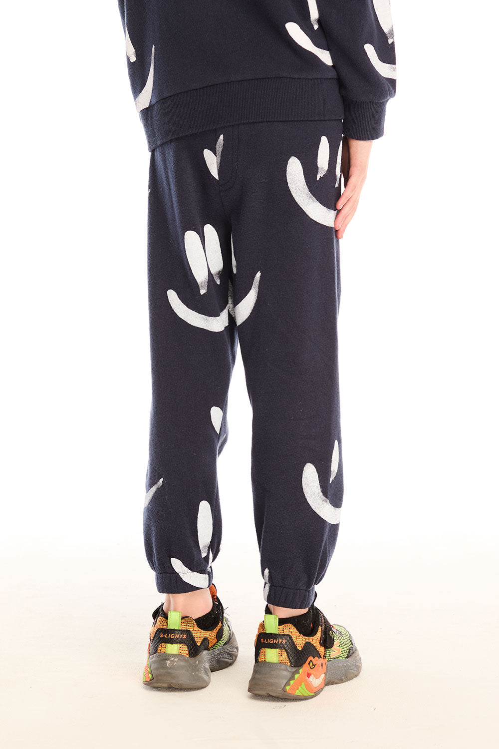 Back view of boy wearing Chaser's navy Allover Smileys Pants with white patterns on a white background