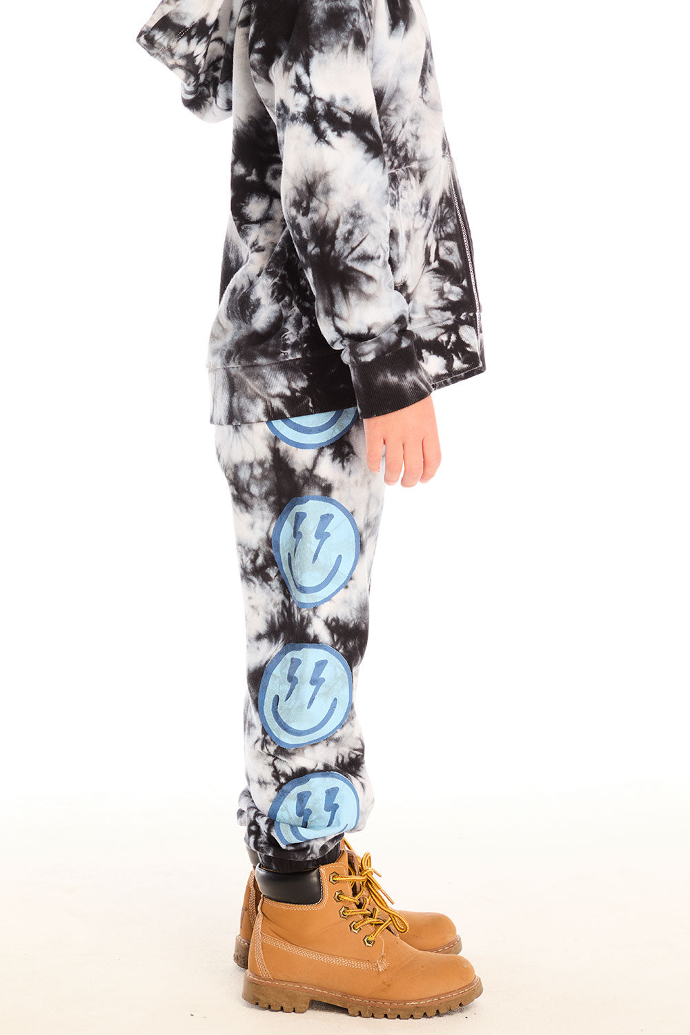 Side view of boy wearing Chaser’s Smiley Bolt tie-dye pants with and matching hoodie on a white background