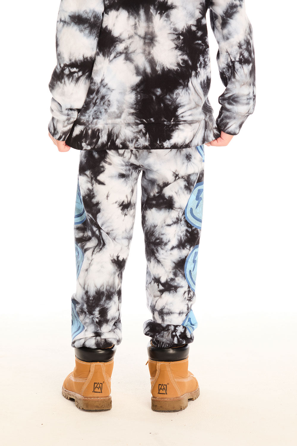 Back view of boy wearing Chaser’s Smiley Bolt tie-dye pants with matching hoodie on a white background