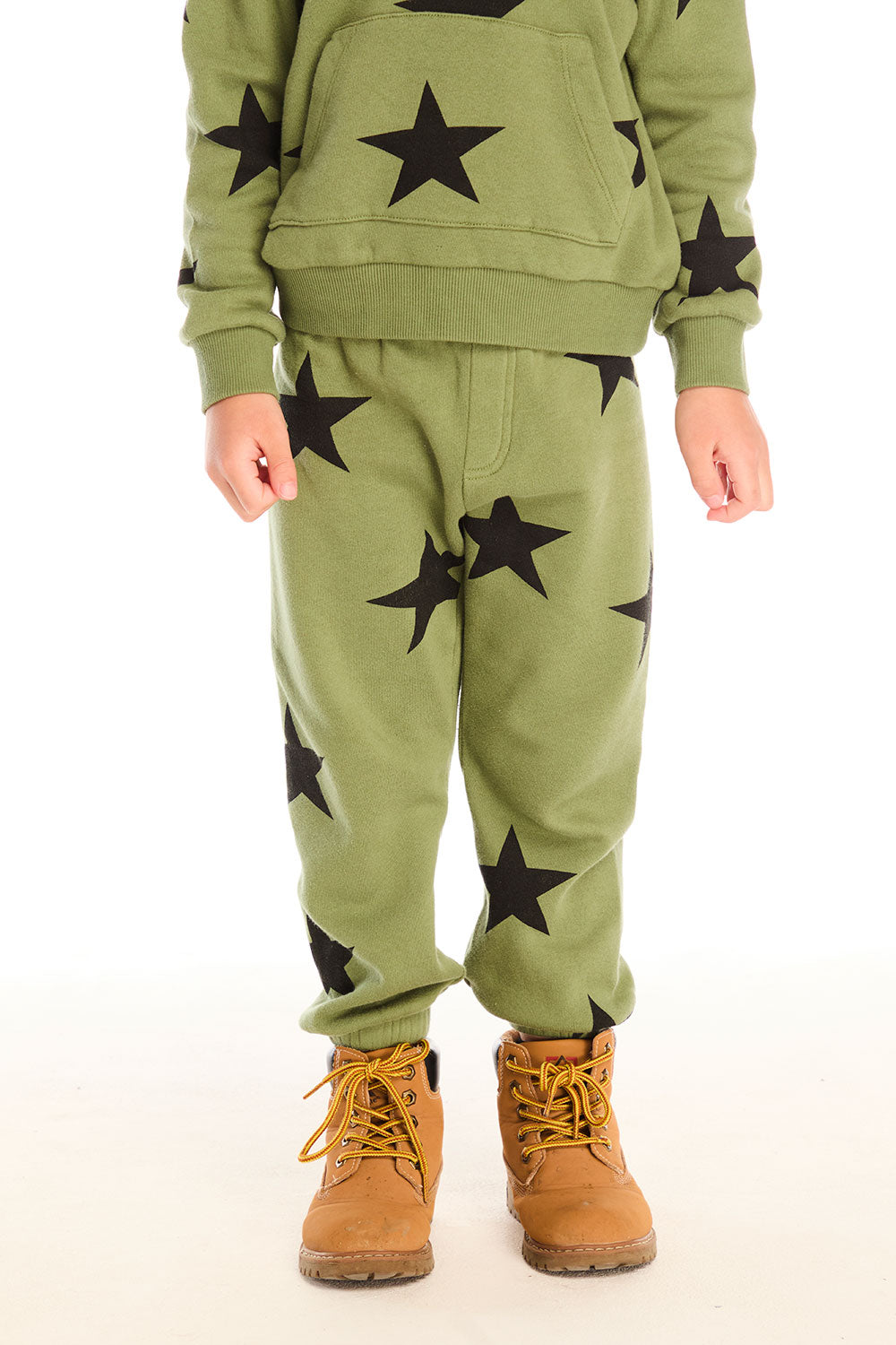 A boy wearing Chaser's Allover Stars green pant with black star patterns on a white background