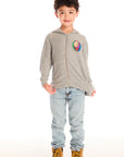 Full body view of boy wearing Chaser’s The Grateful Dead Colorblocked Stealie heather grey zip up hoodie with colorful Steal Your Face logo, light blue jeans, and brown boots on a white background