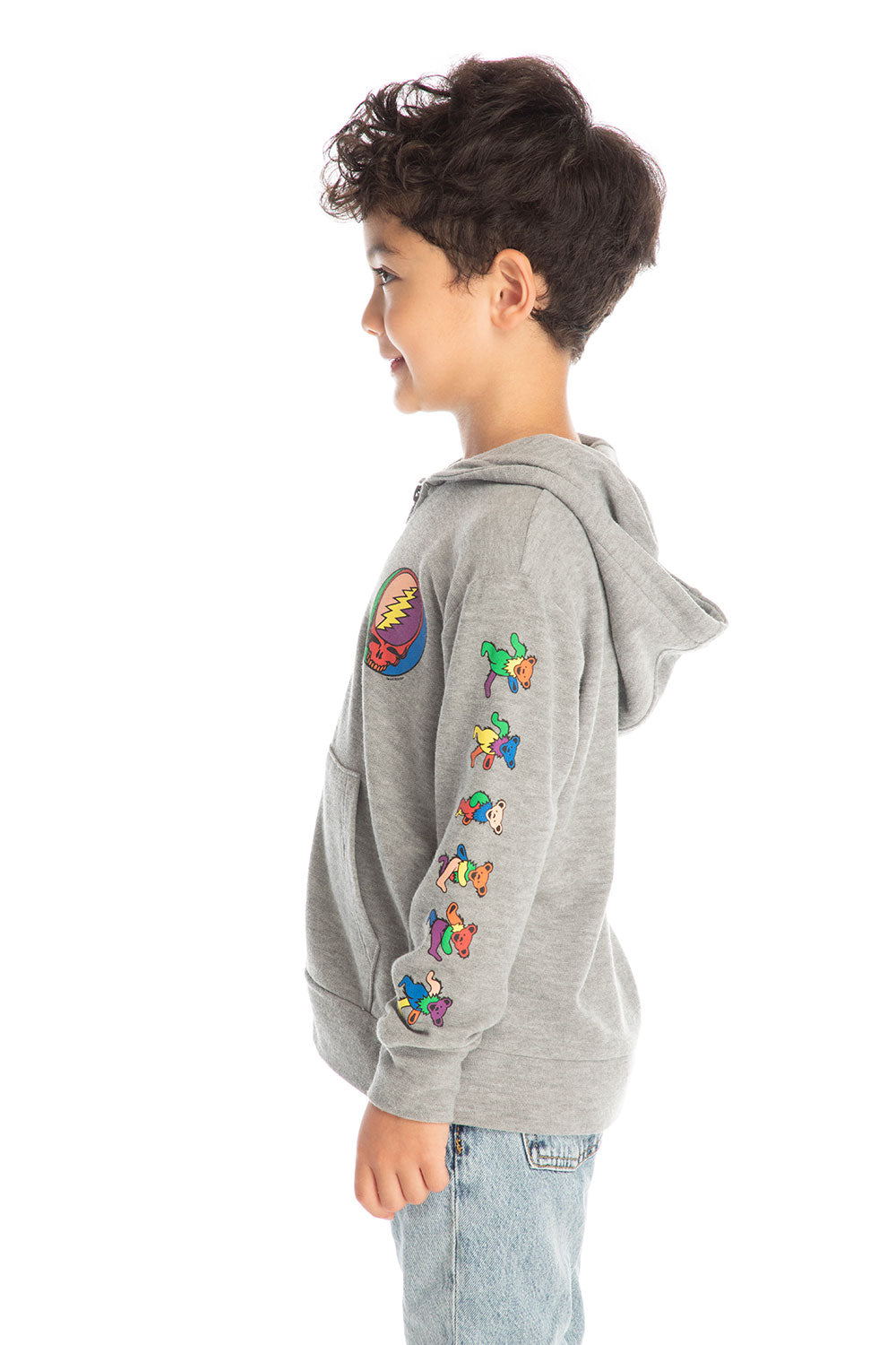Side view of boy wearing Chaser’s The Grateful Dead Colorblocked Stealie heather grey zip up hoodie featuring colorful Dancing Bears on the sleeve, paired with light blue jeans and brown boots on a white background