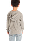 Back view of boy wearing Chaser’s The Grateful Dead Colorblocked Stealie heather grey zip up hoodie, light blue jeans, and brown boots on a white background