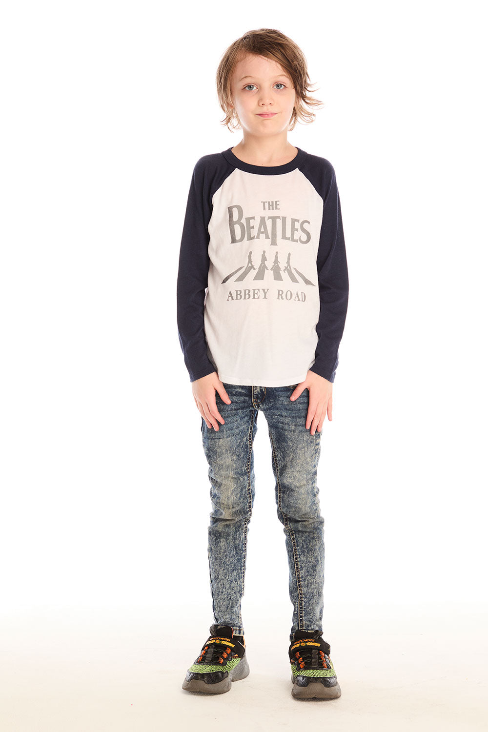 Full body view of boy wearing Chaser’s The Beatles Abbey Road football tee in white with navy blue sleeves and jeans on a white background