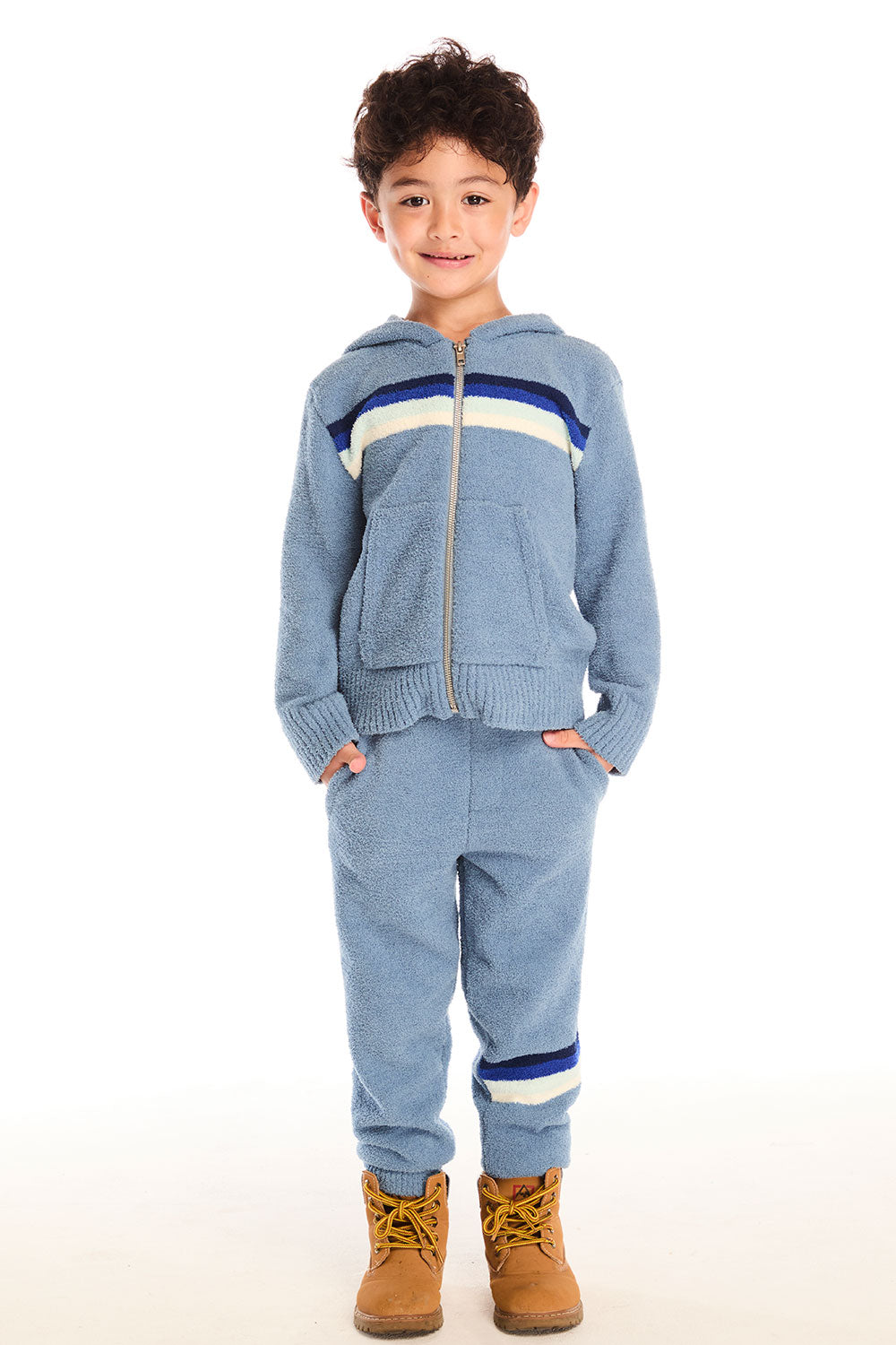 Full body view of boy wearing Chaser’s Lounge Tahoe Blue Pant with Pocket featuring dark blue and white color block on the left leg, styled with matching zip up hoodie and brown boots on a white background
