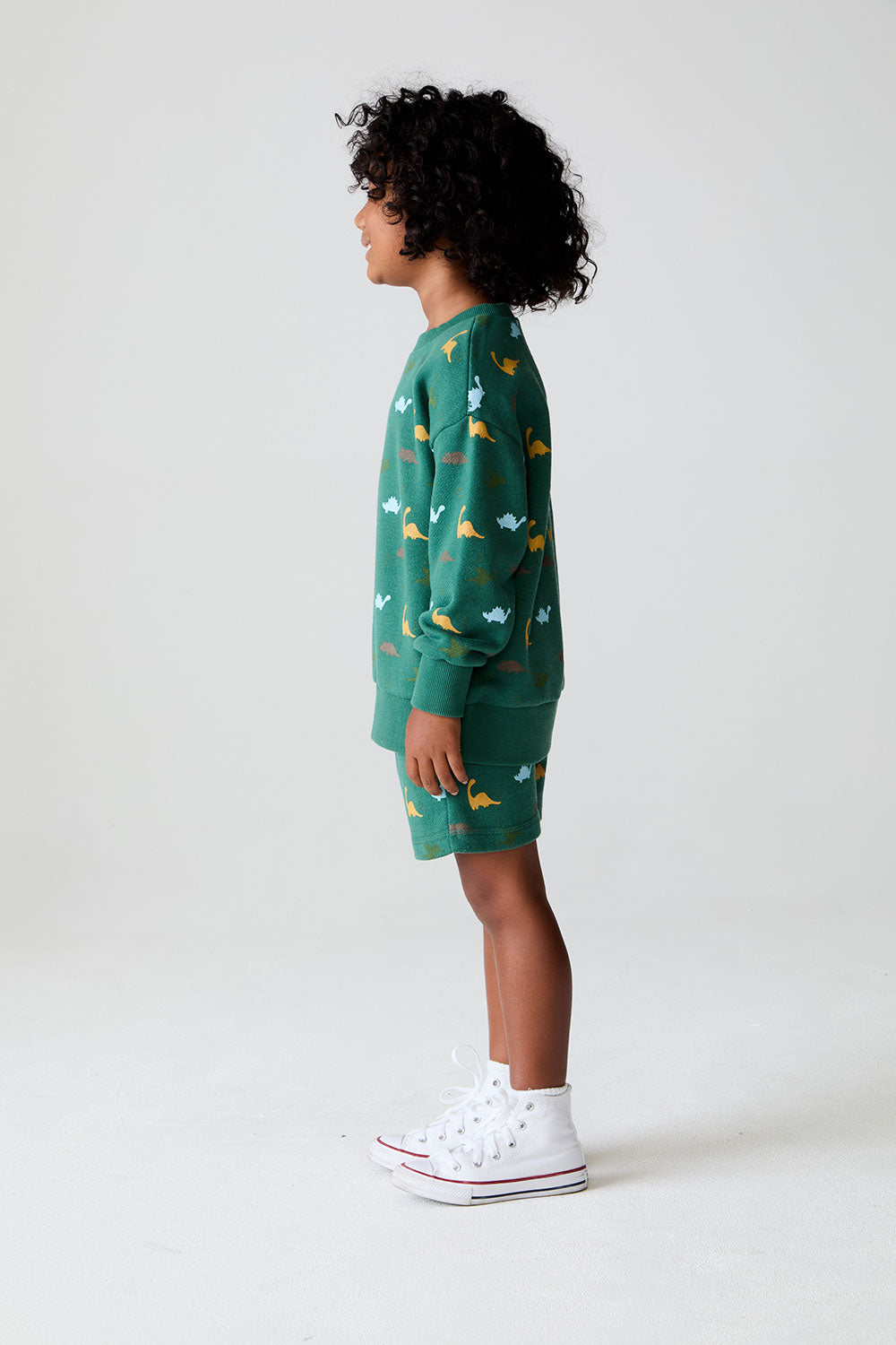 Side view of boy wearing Chaser's green Dino Party Shorts and matching Pullover against a white background