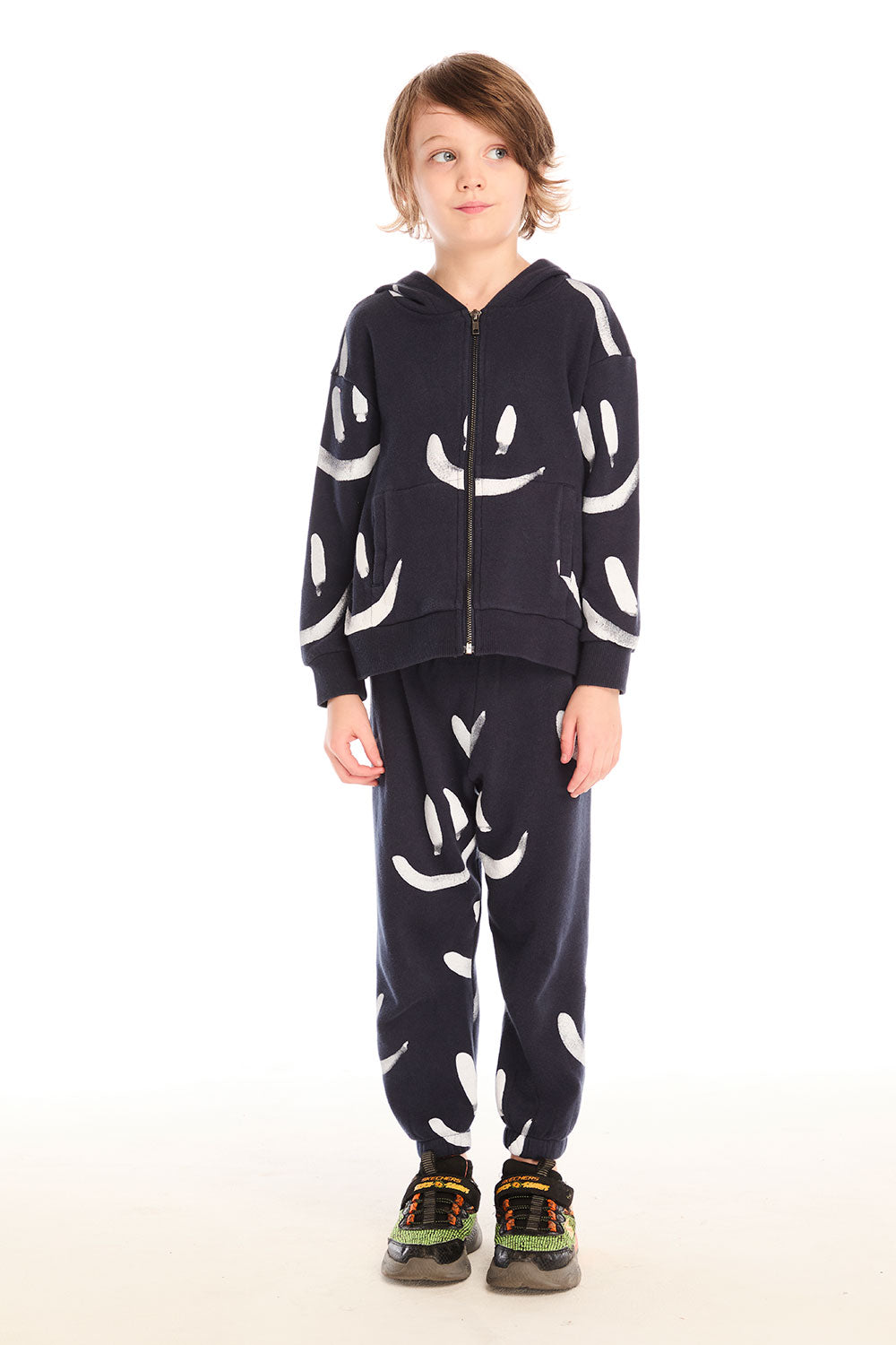 Full body view of boy wearing Chaser’s Smileys navy blue zip up hoodie with white smiley face patterns and matching pants on a white background