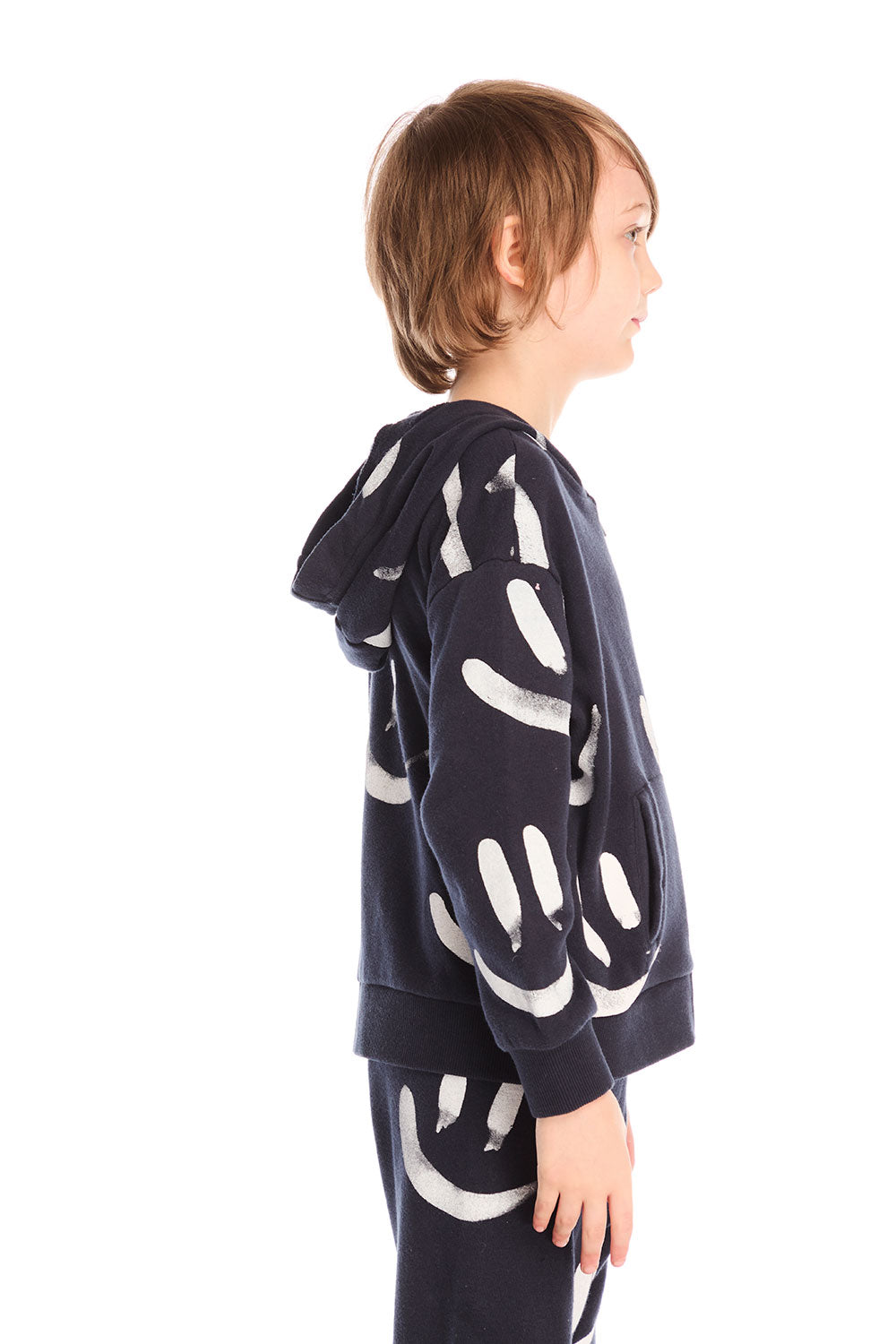 Side view of boy wearing Chaser’s Smileys navy blue zip up hoodie with white smiley face graphics against a white background