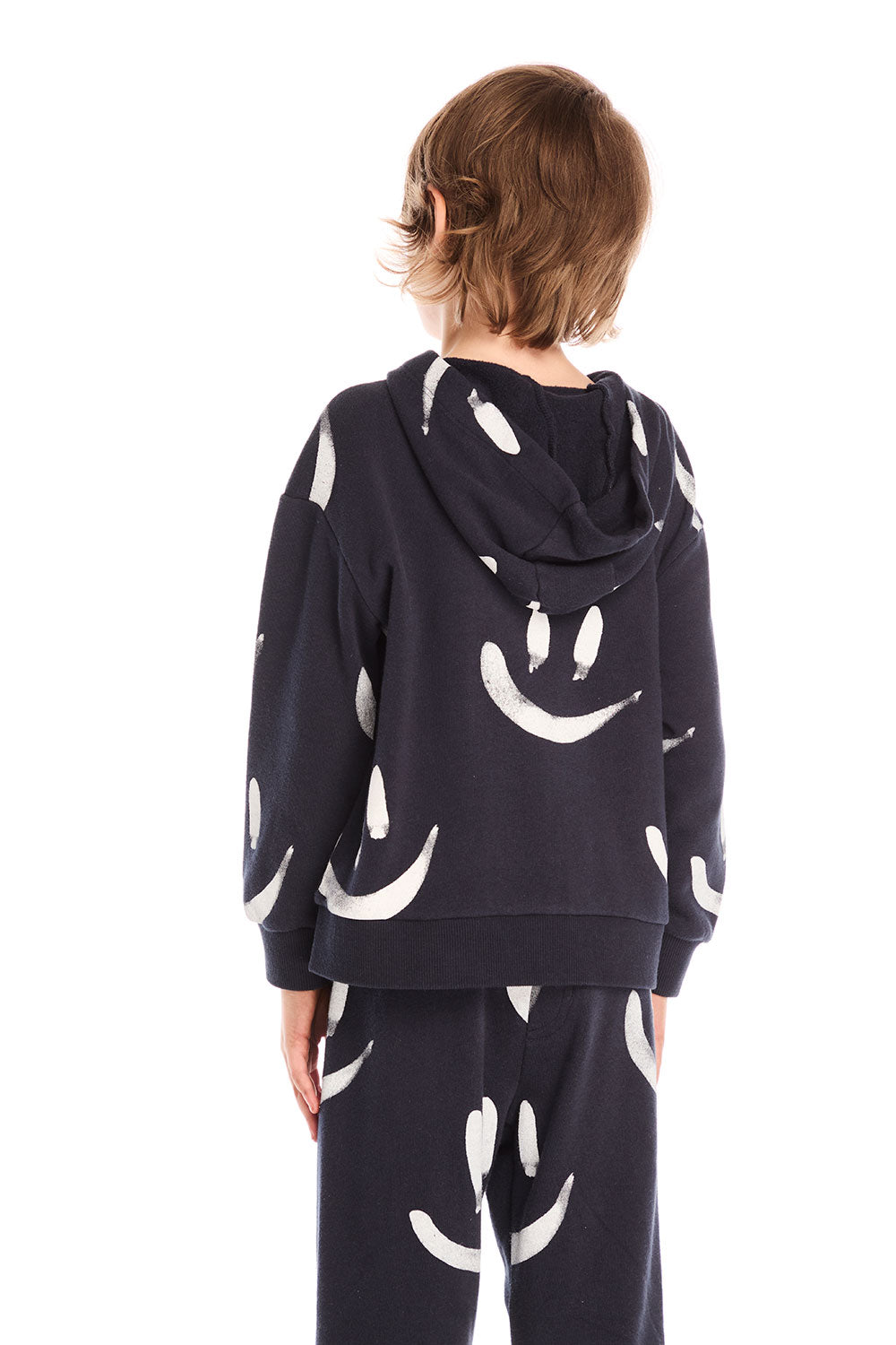 Back view of boy wearing Chaser’s Smileys navy blue zip up hoodie with allover white smiley face print against a white background