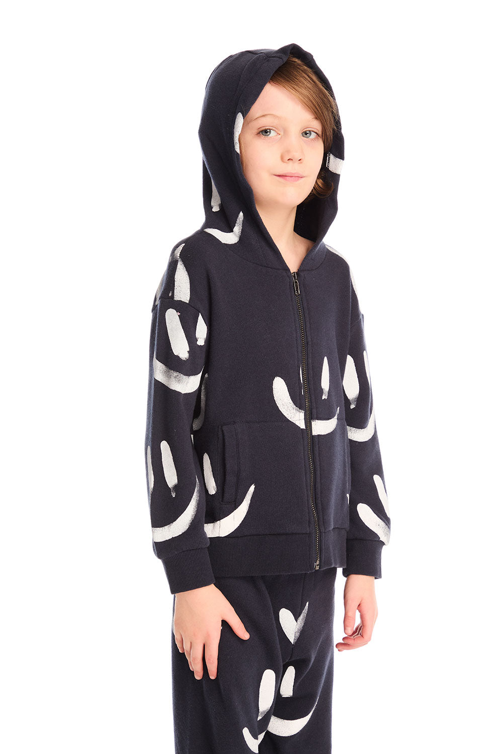 Boy wearing Chaser’s Smileys navy blue zip up hoodie and hood up with white smiley face patterns and matching pants on a white background